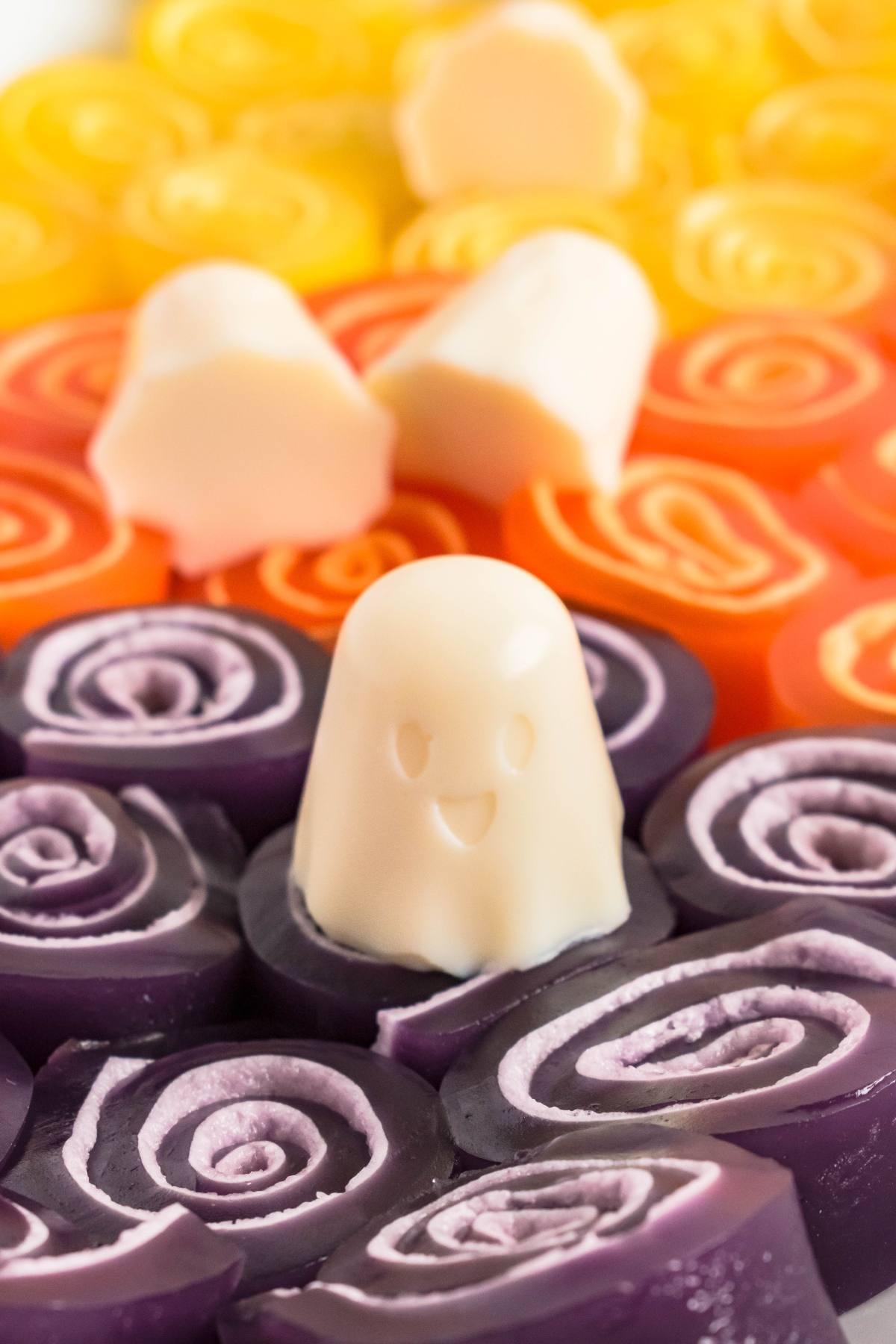 Cute white ghost-shaped candy among colorful orange, yellow, and purple swirled jelly candies.