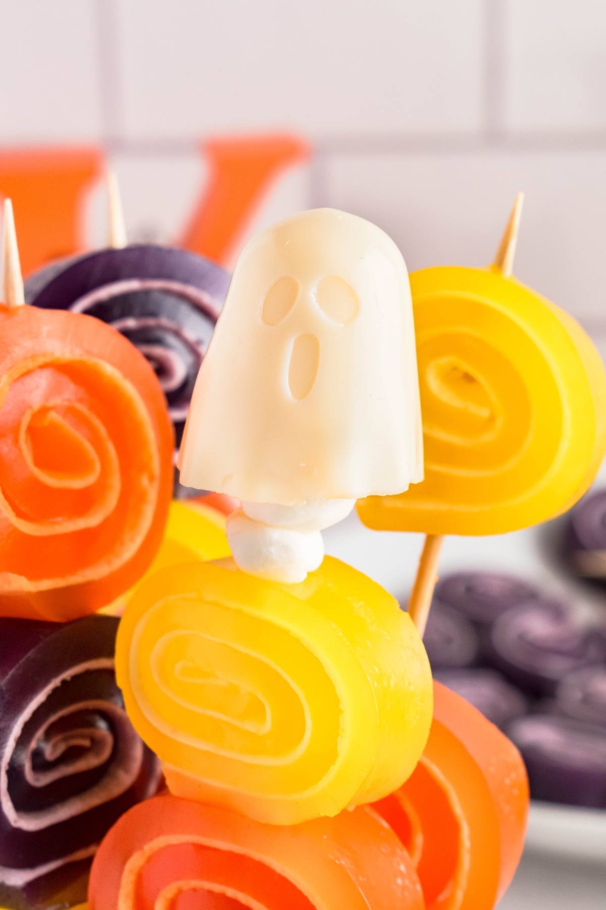 Colorful fruit roll-up spirals on skewers with a white candy ghost on top, arranged for a festive display.