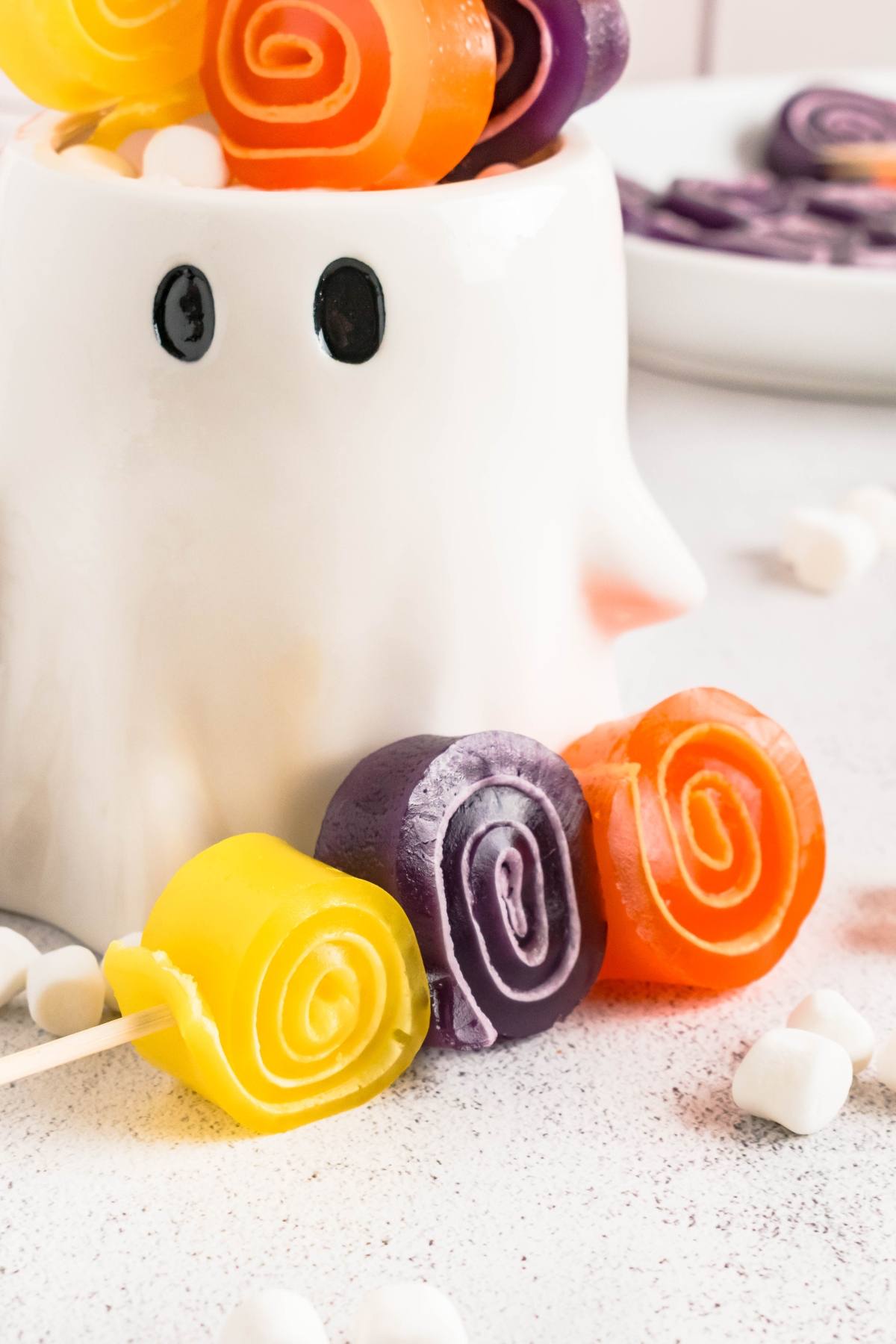 Colorful spiral candies and marshmallows in front of a white ghost-shaped container with black eyes.