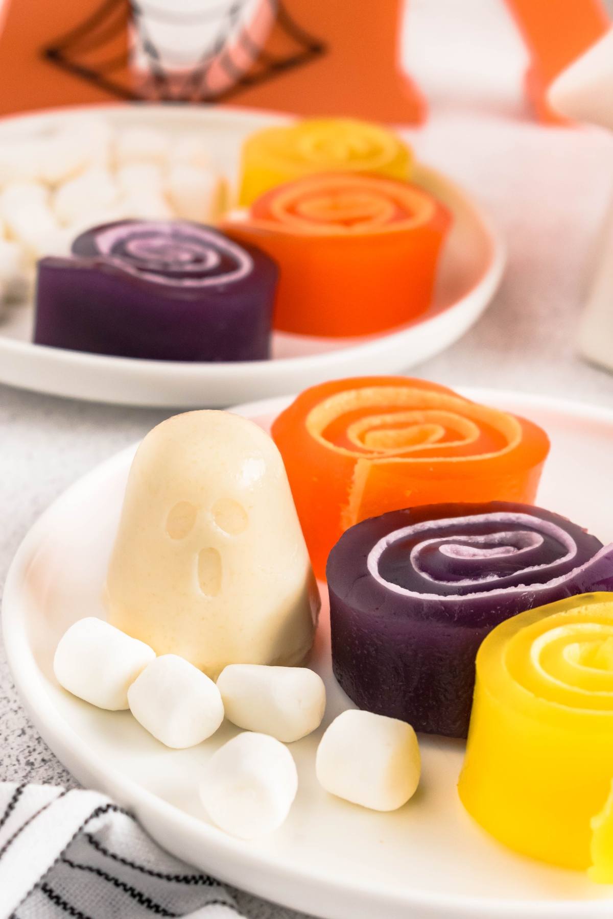 Colorful candy rolls and a ghost-shaped marshmallow on a plate, surrounded by mini marshmallows.