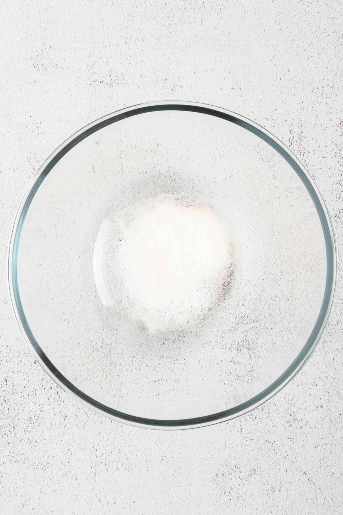 A glass mixing bowl with a mound of white powder on a light gray surface.