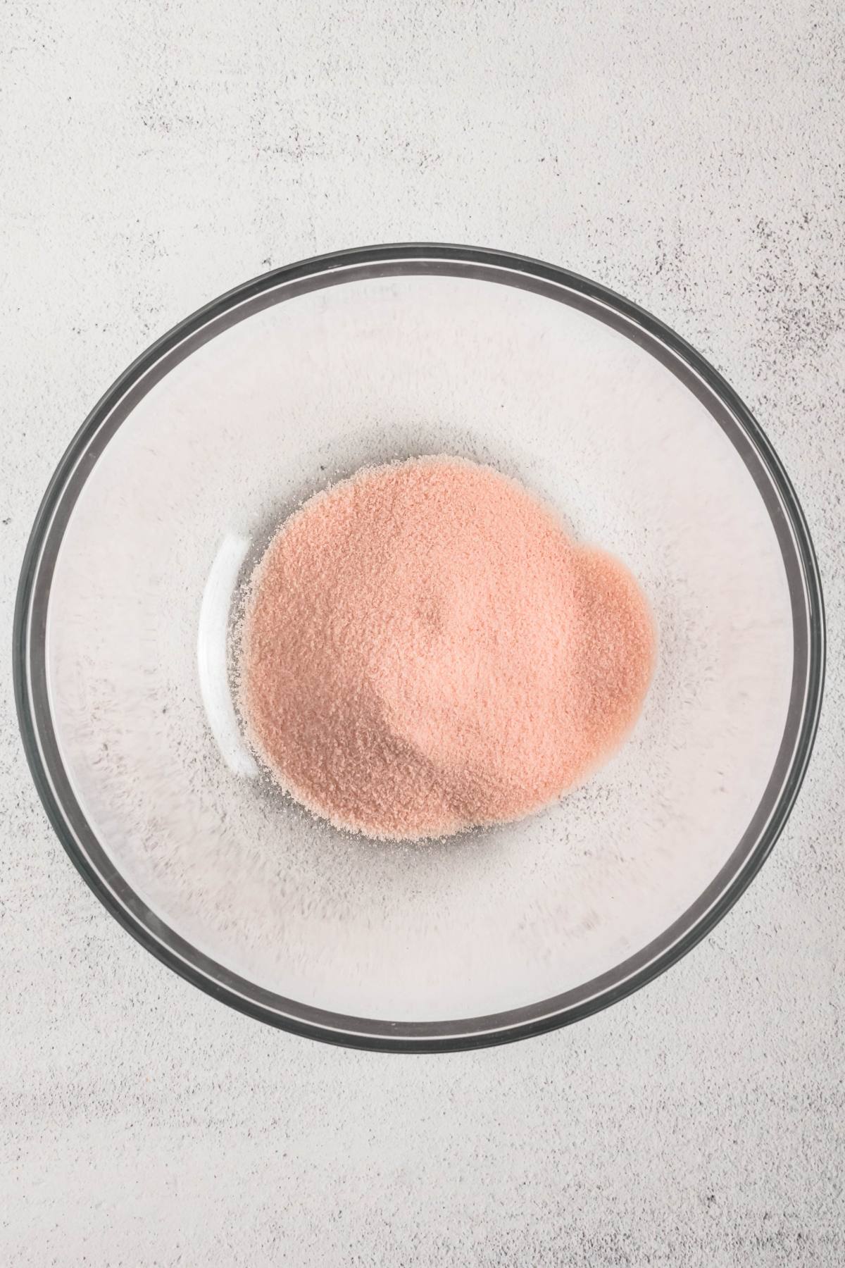 A glass bowl filled with a mound of pink powder on a light-colored surface.
