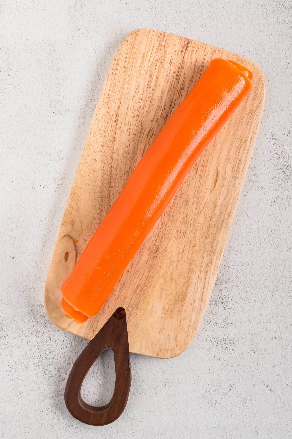 An orange roll of fruit leather on a wooden cutting board with a dark handle.