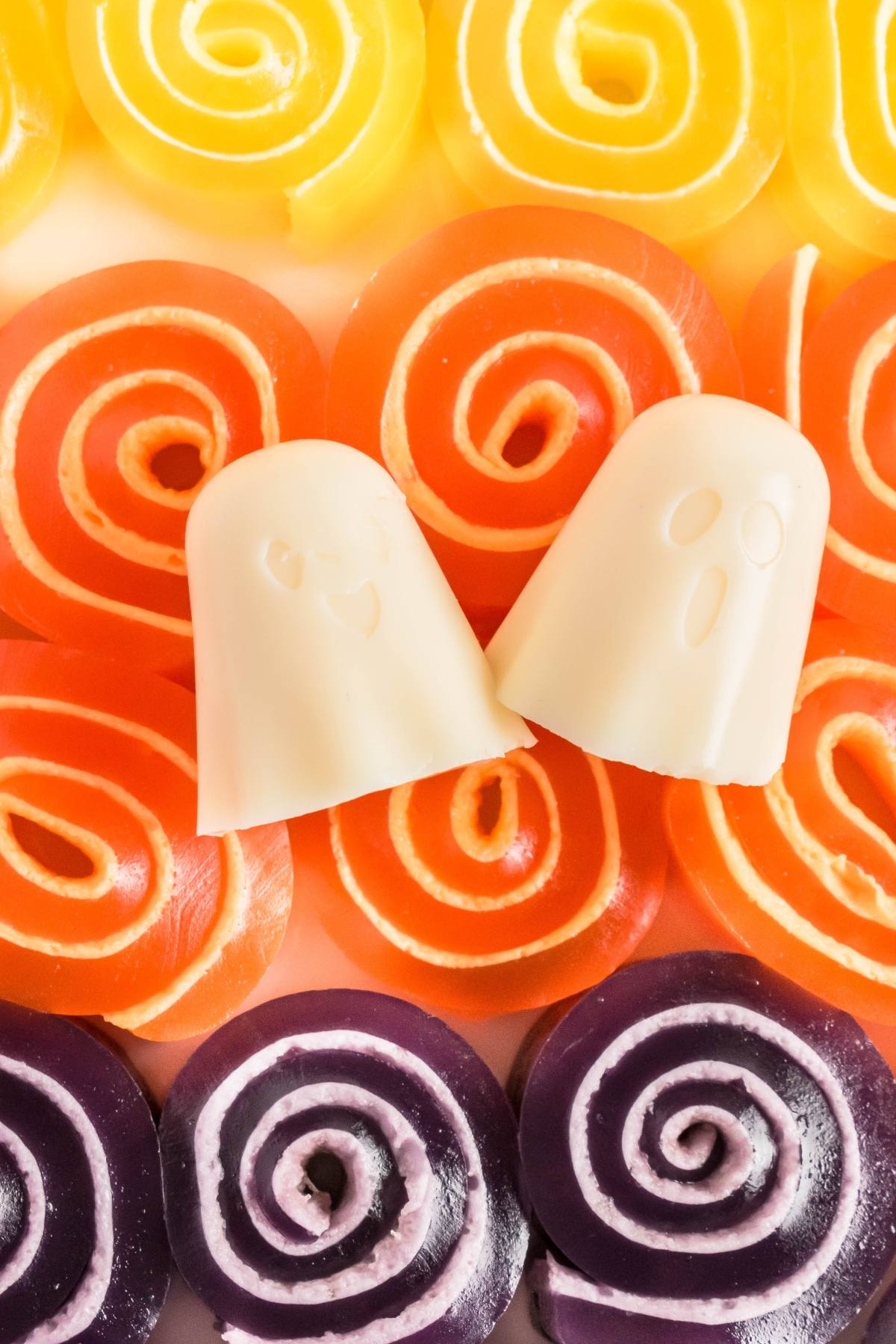 Two white ghost-shaped candies on orange swirled candy rolls, with yellow and purple rolls above and below.