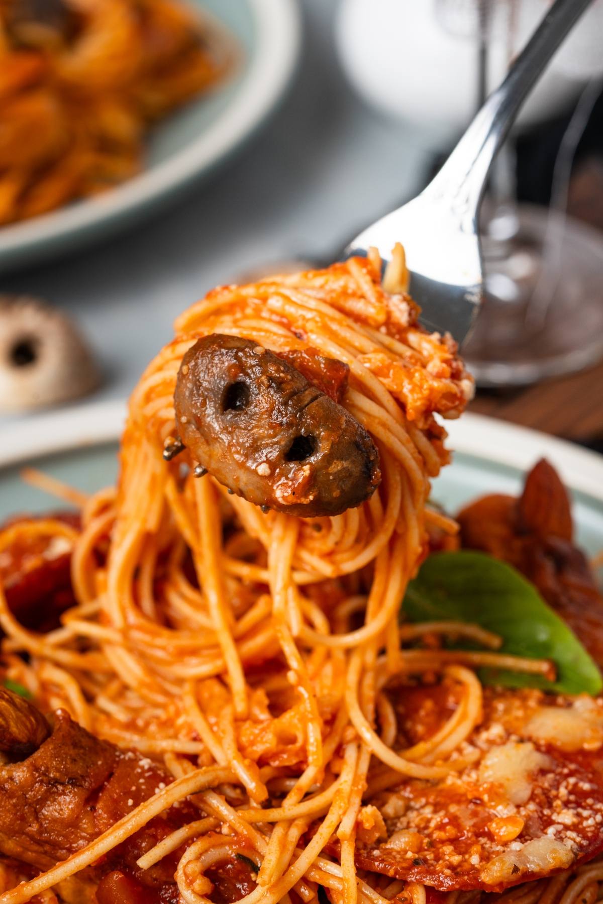 A fork twirls spaghetti with tomato sauce, mushrooms, and basil over a plate of pasta.