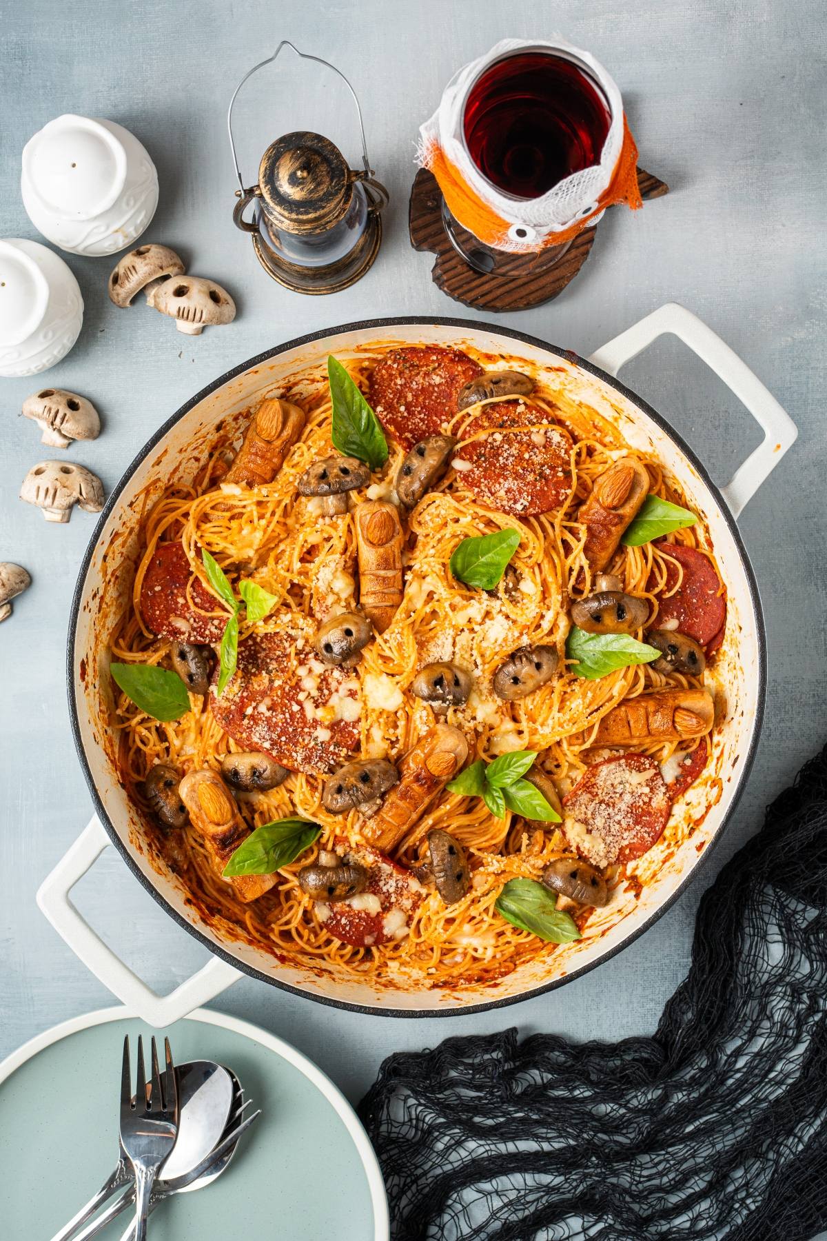Spaghetti in tomato sauce with sausage "fingers," olives, basil, and cheese in a white pan, Halloween-themed.