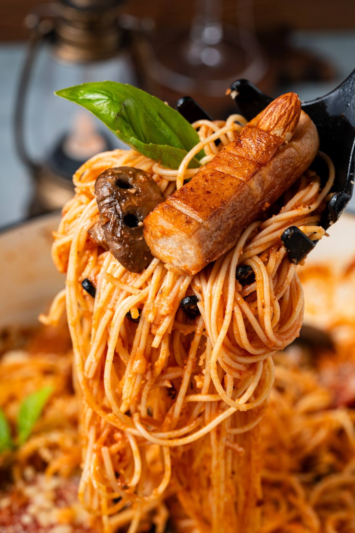 Spaghetti with tomato sauce, olives, and a sausage made to look like a finger, garnished with basil.
