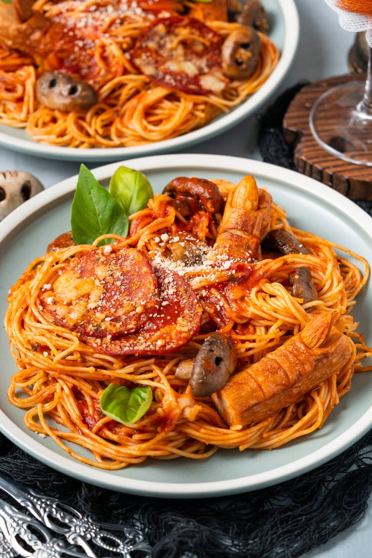 Spaghetti with tomato sauce, sliced sausage, olives, and sausage fingers, garnished with basil on a plate.