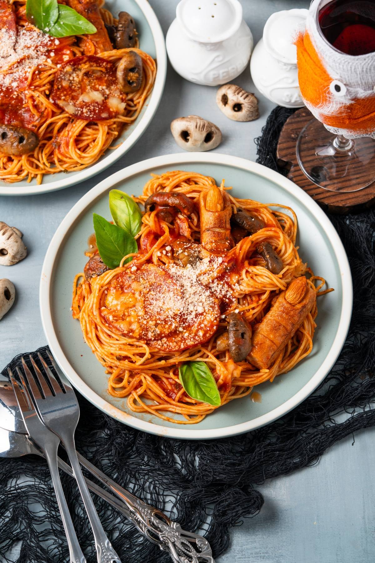 Plate of spaghetti with tomato sauce, mushrooms, parmesan, basil, and Halloween finger-shaped breadsticks.