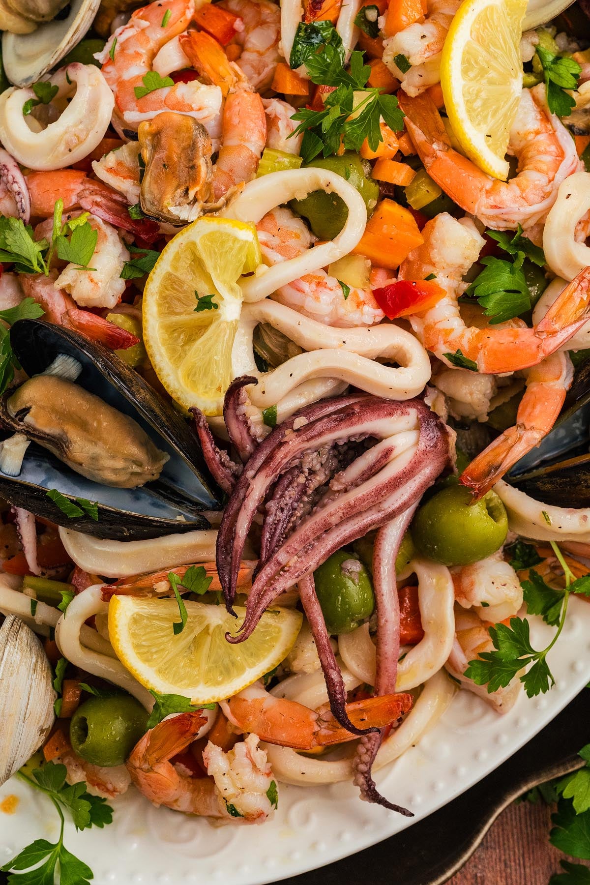 Italian Seafood Salad with shrimp, squid, mussels, olives, chopped vegetables, parsley, and lemon slices.