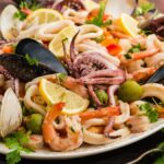 A platter of Italian Seafood Salad with shrimp, mussels, clams, squid, olives, and lemon wedges.