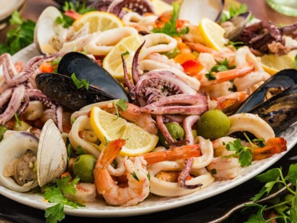 A platter of Italian Seafood Salad with shrimp, mussels, clams, squid, olives, and lemon wedges.