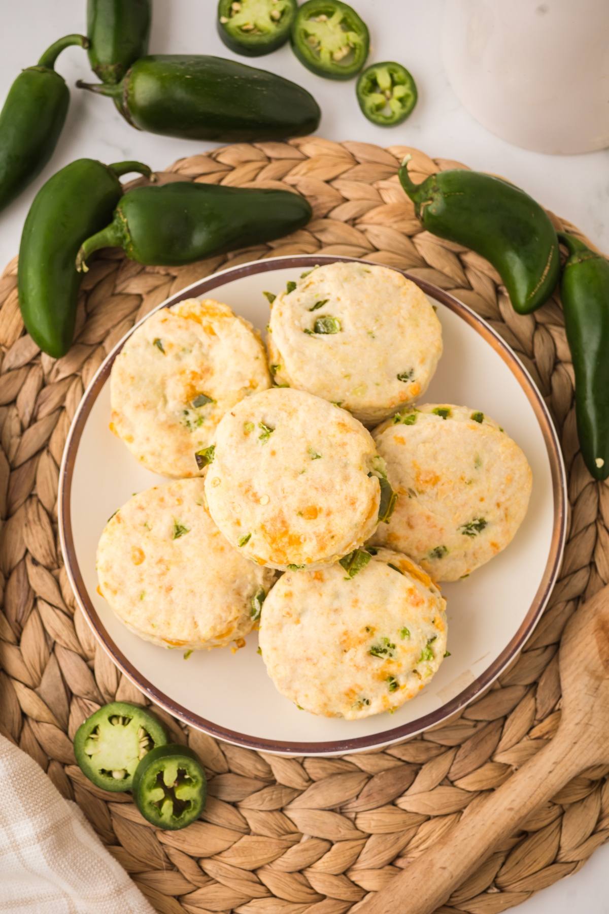 A plate of biscuits with chopped jalapeños and cheese, surrounded by whole and sliced jalapeños.
