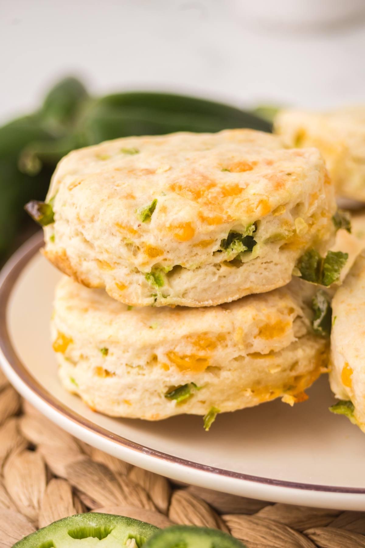 Two cheddar and jalapeño biscuits stacked on a plate, with jalapeño slices in the background.