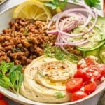 A bowl with creamy hummus, spiced ground lamb, cucumber, tomato, red onion, lemon, and fresh herbs—perfect for delicious lamb hummus bowls.