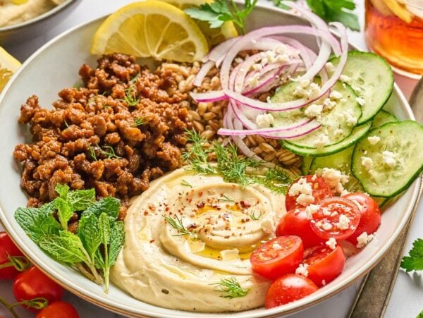 A bowl with creamy hummus, spiced ground lamb, cucumber, tomato, red onion, lemon, and fresh herbs—perfect for delicious lamb hummus bowls.