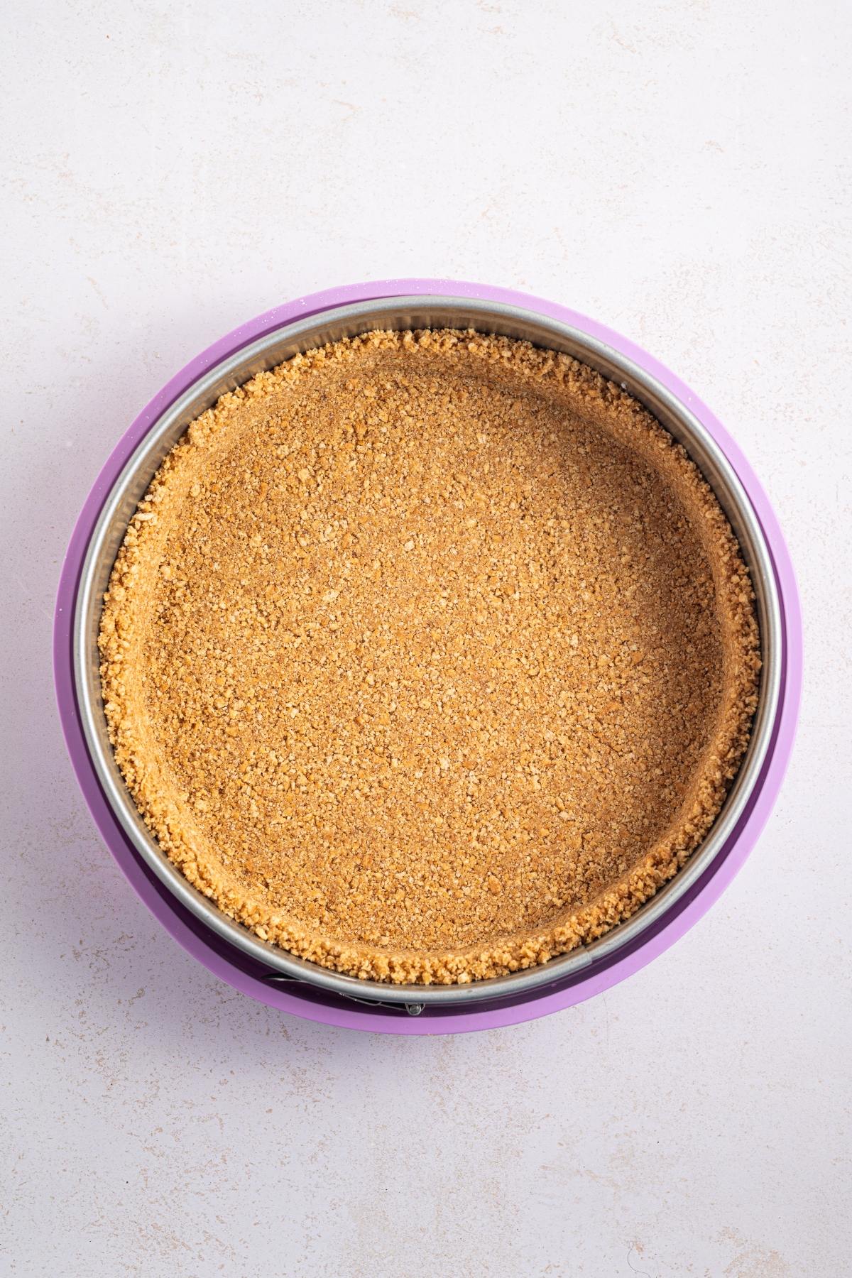 A round pan with an even layer of graham cracker crust pressed on the bottom and sides.