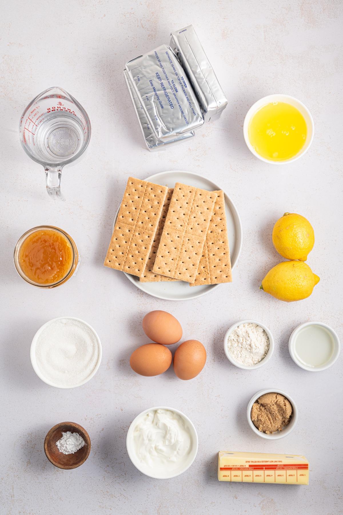 Baking ingredients including graham crackers, eggs, lemons, butter, sugar, cream cheese, and measuring tools.