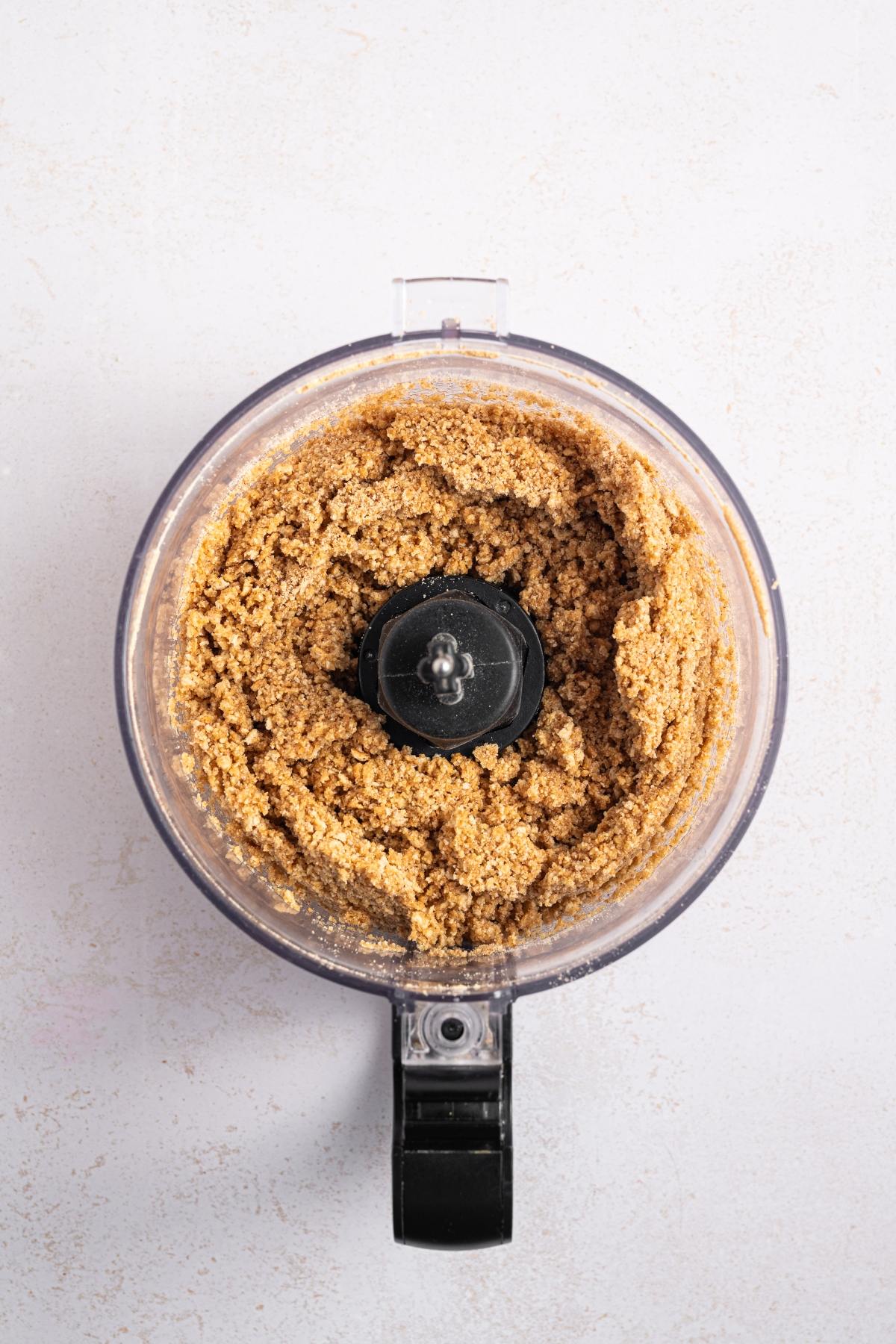 Food processor filled with blended nut mixture, viewed from above on a light surface.