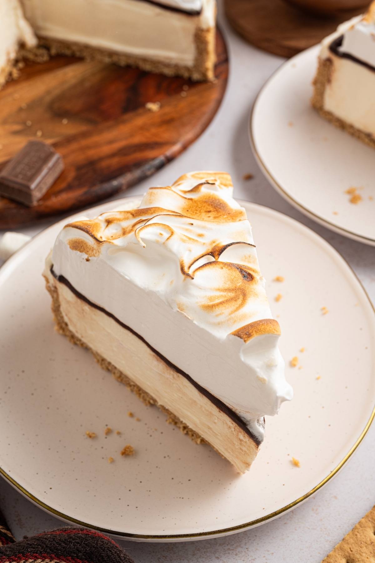 A slice of pie with graham crust, chocolate, creamy filling, and toasted meringue on a white plate.