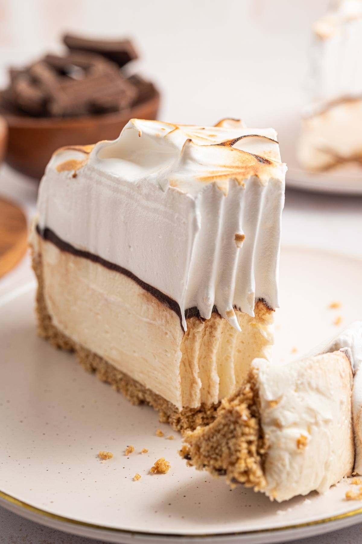 A slice of creamy pie with a graham crust, chocolate layer, and toasted meringue topping on a plate.