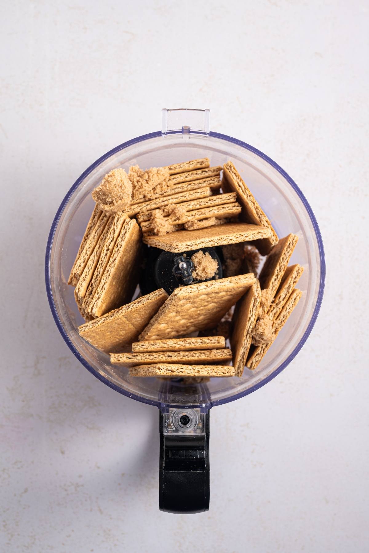 A food processor bowl filled with whole graham crackers, ready to be crushed.