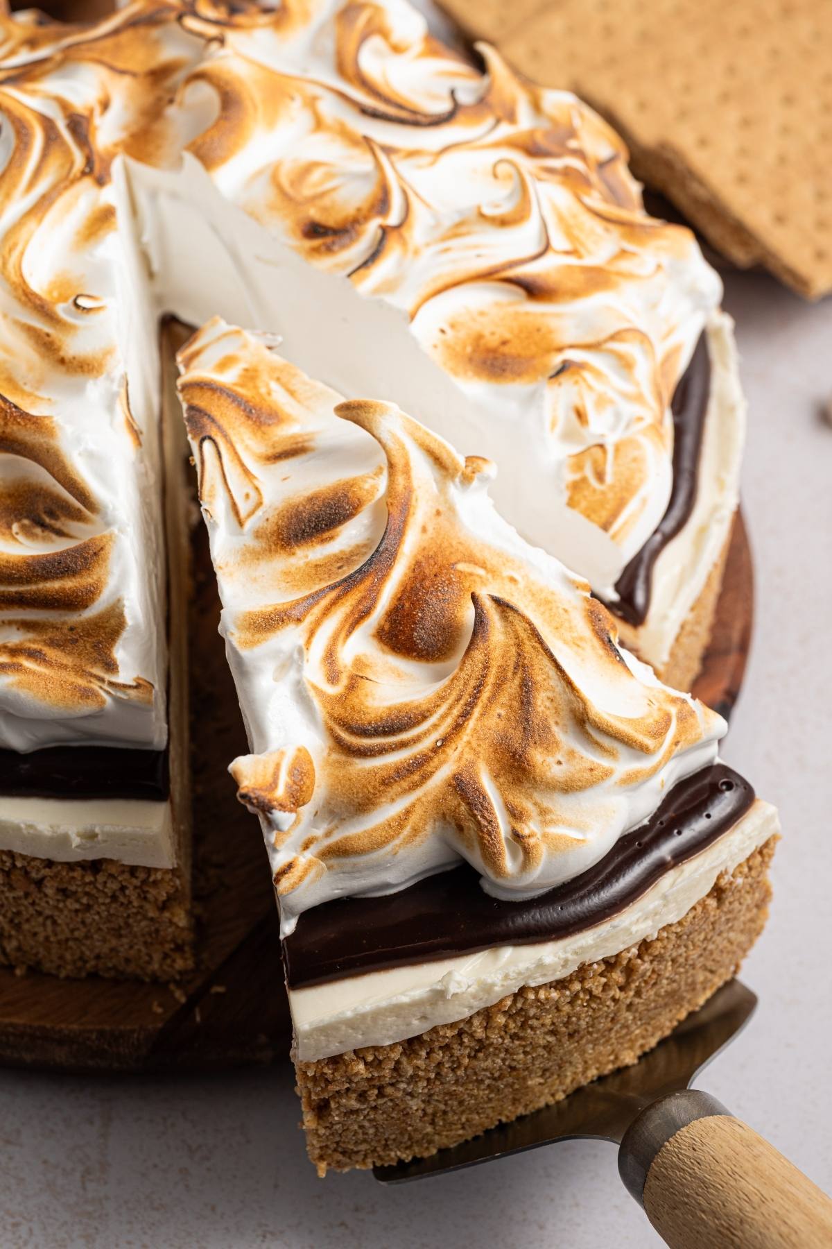 A slice of toasted meringue-topped pie with a graham cracker crust being served from the whole pie.