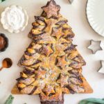 Nutella Puff Pastry Christmas Tree dusted with powdered sugar, shaped like a festive tree and surrounded by baking tools and decorations.