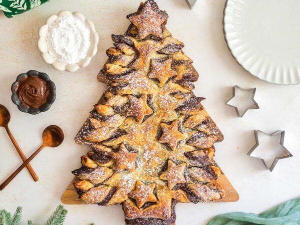 Nutella Puff Pastry Christmas Tree dusted with powdered sugar, shaped like a festive tree and surrounded by baking tools and decorations.