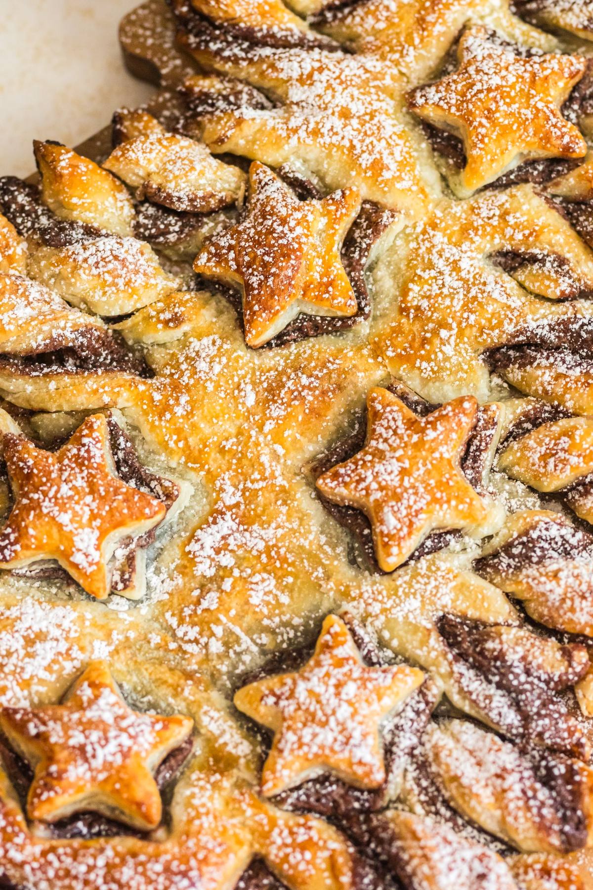 Star-shaped pastries dusted with powdered sugar, arranged in a festive pattern on a baked surface.