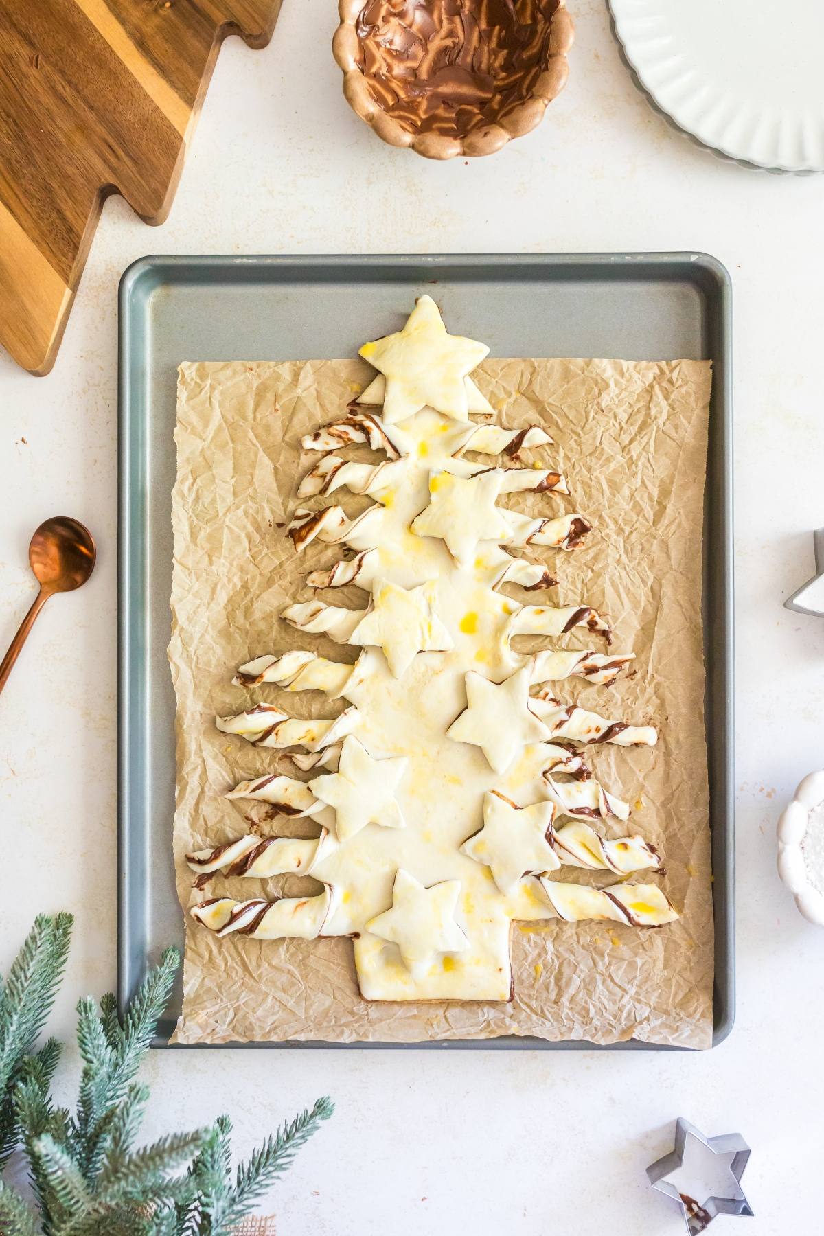 A Christmas tree-shaped pastry with star cutouts on a baking tray lined with parchment paper.