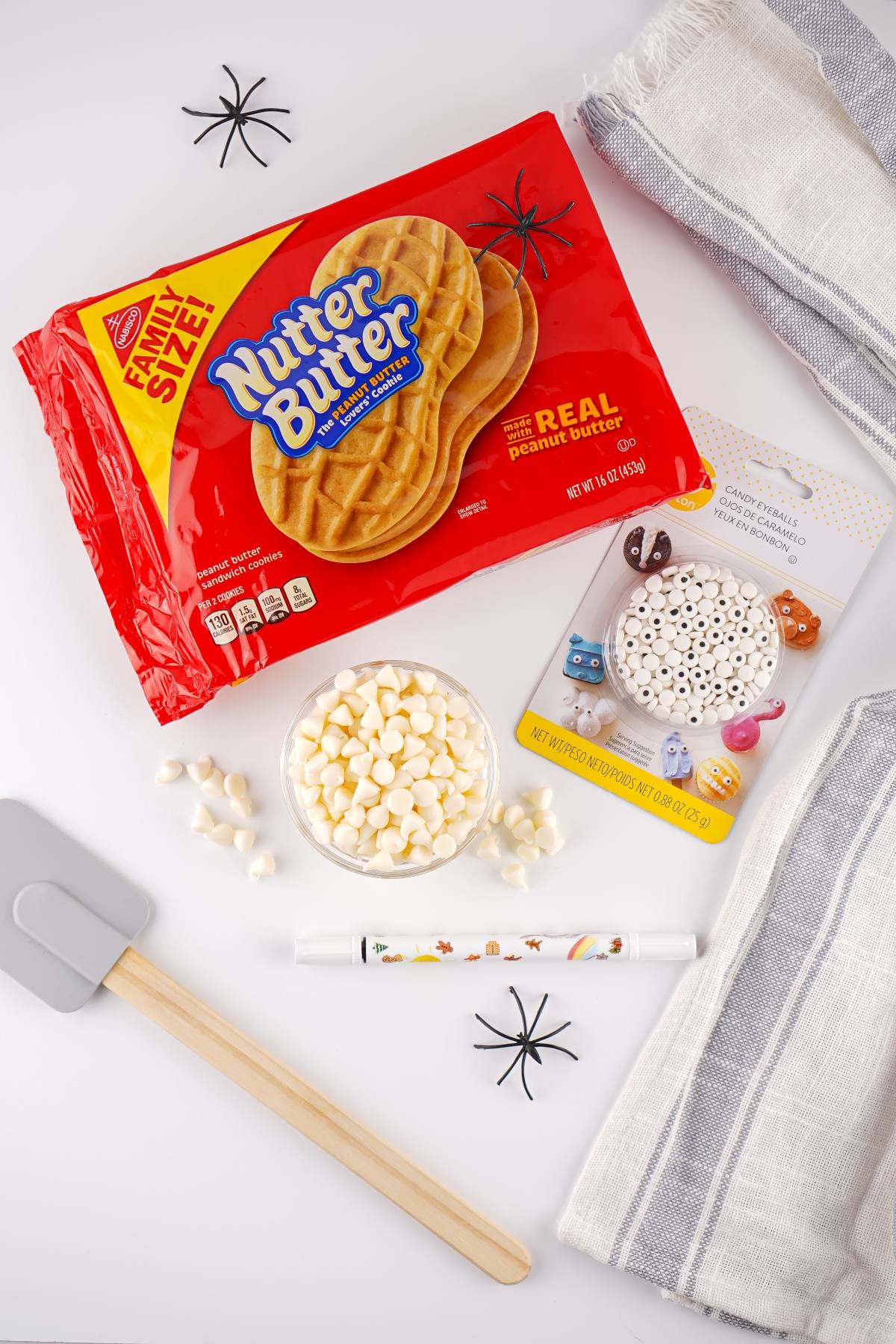 Nutter Butter cookies, white chocolate chips, candy eyes, marker, utensils, and towels on a white surface.