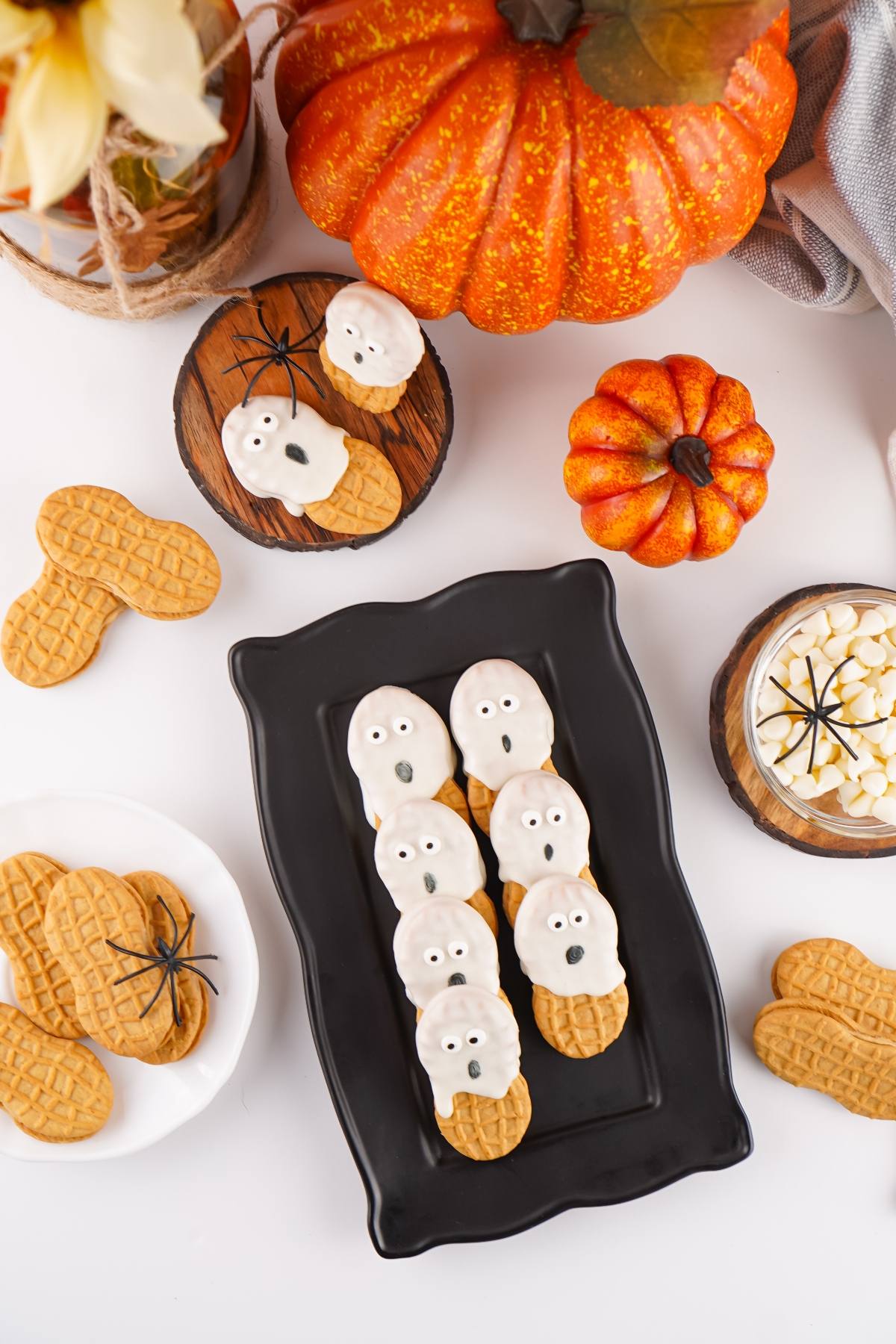 Nutter Butter cookies decorated as ghosts on a black tray, with pumpkins and candy on the table.