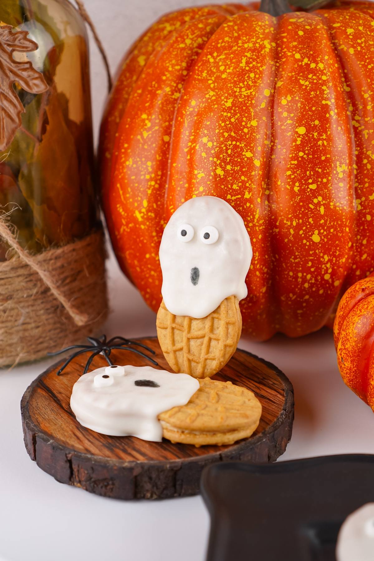 Nutter Butter cookies decorated as ghosts with white icing, in front of a large orange pumpkin.