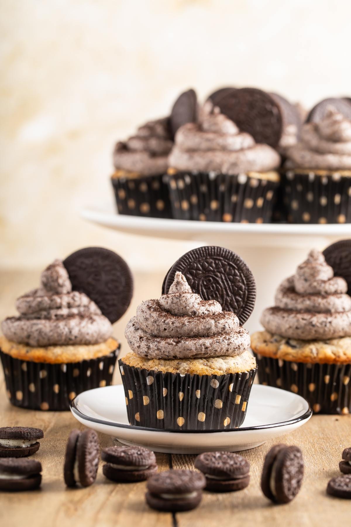 Vanilla cupcakes with cookies and cream frosting, topped with chocolate sandwich cookies, on plates and a wooden table.
