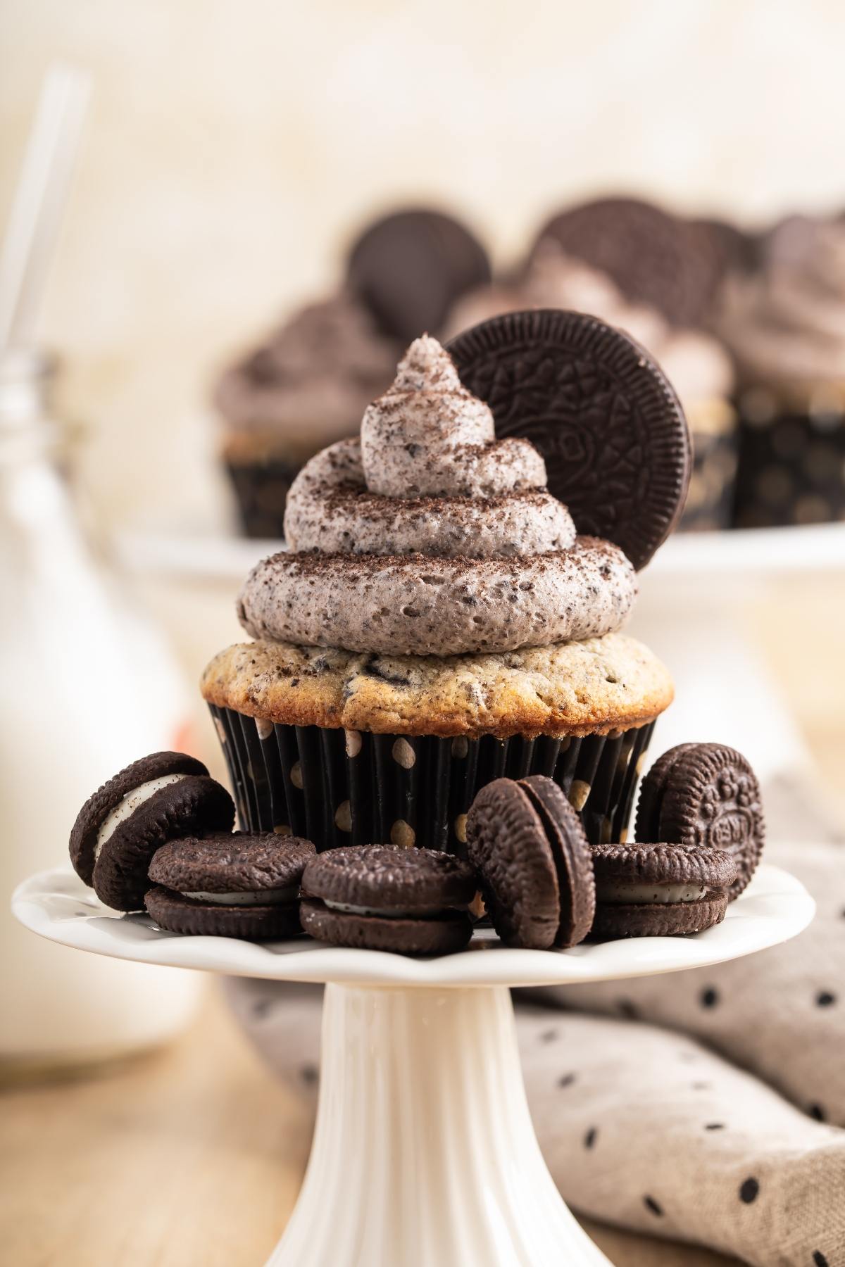 Cupcake with cookies and cream frosting, topped with an Oreo cookie, surrounded by mini Oreo cookies.