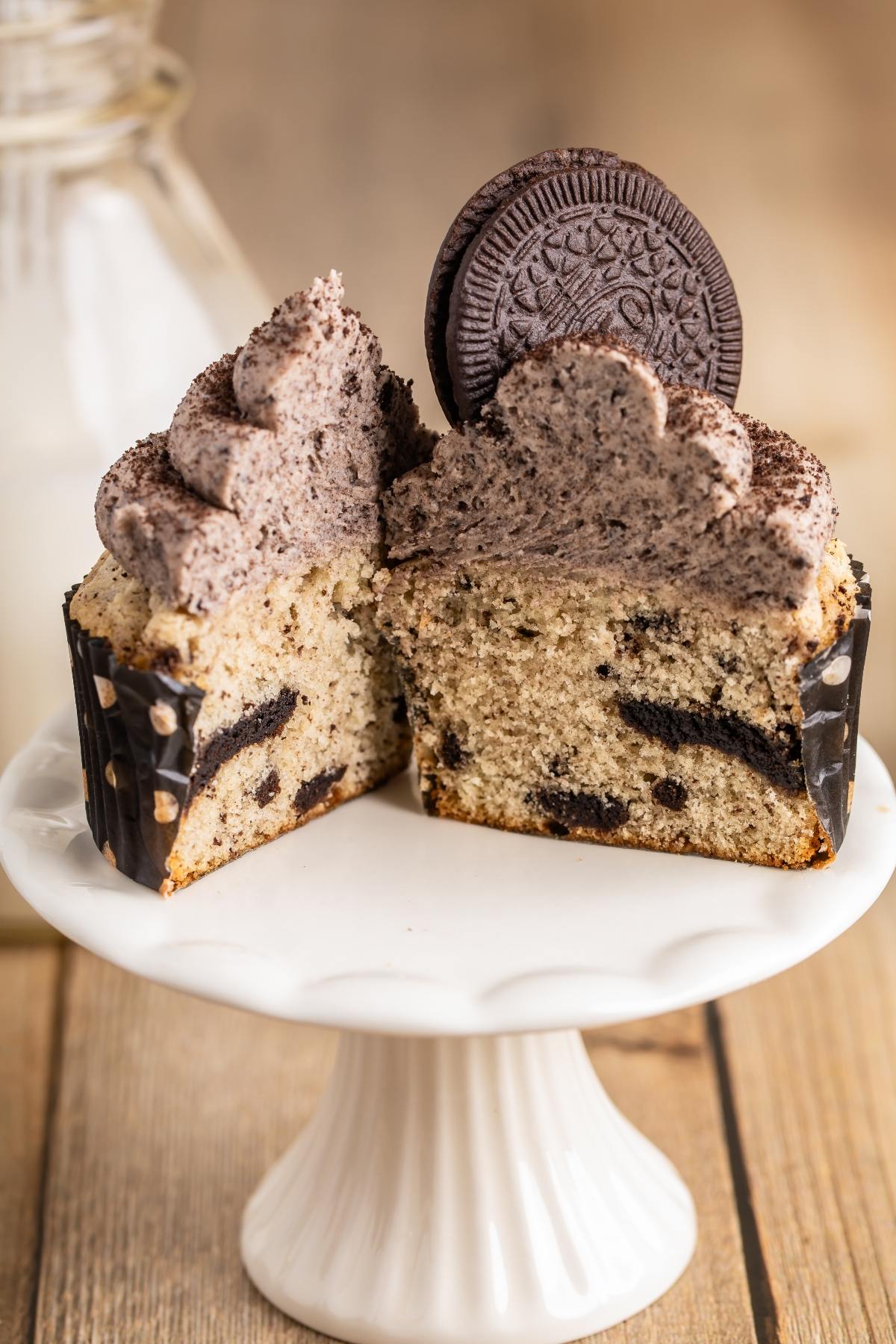 Cookies and cream cupcake cut in half, topped with cookies and cream frosting and a cookie on a white stand.