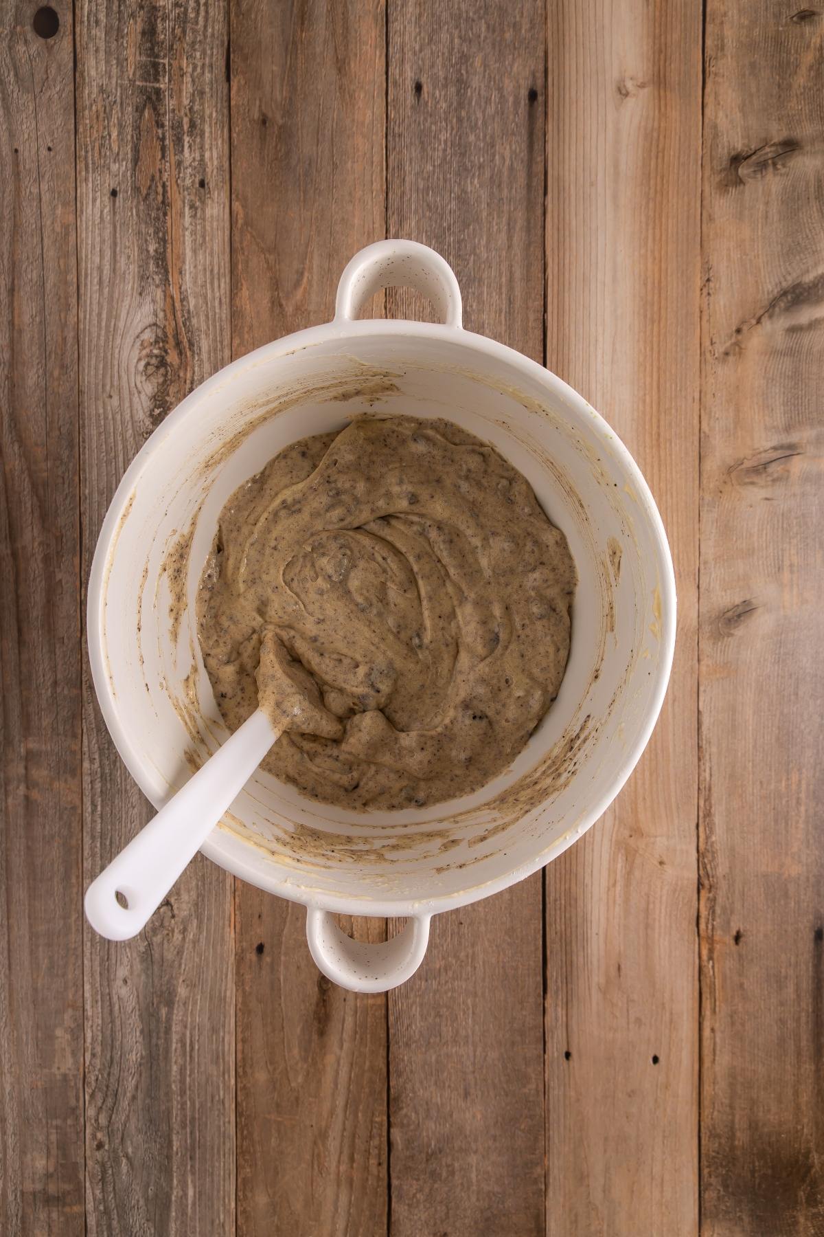 A white mixing bowl with batter and a white spatula on a wooden surface.