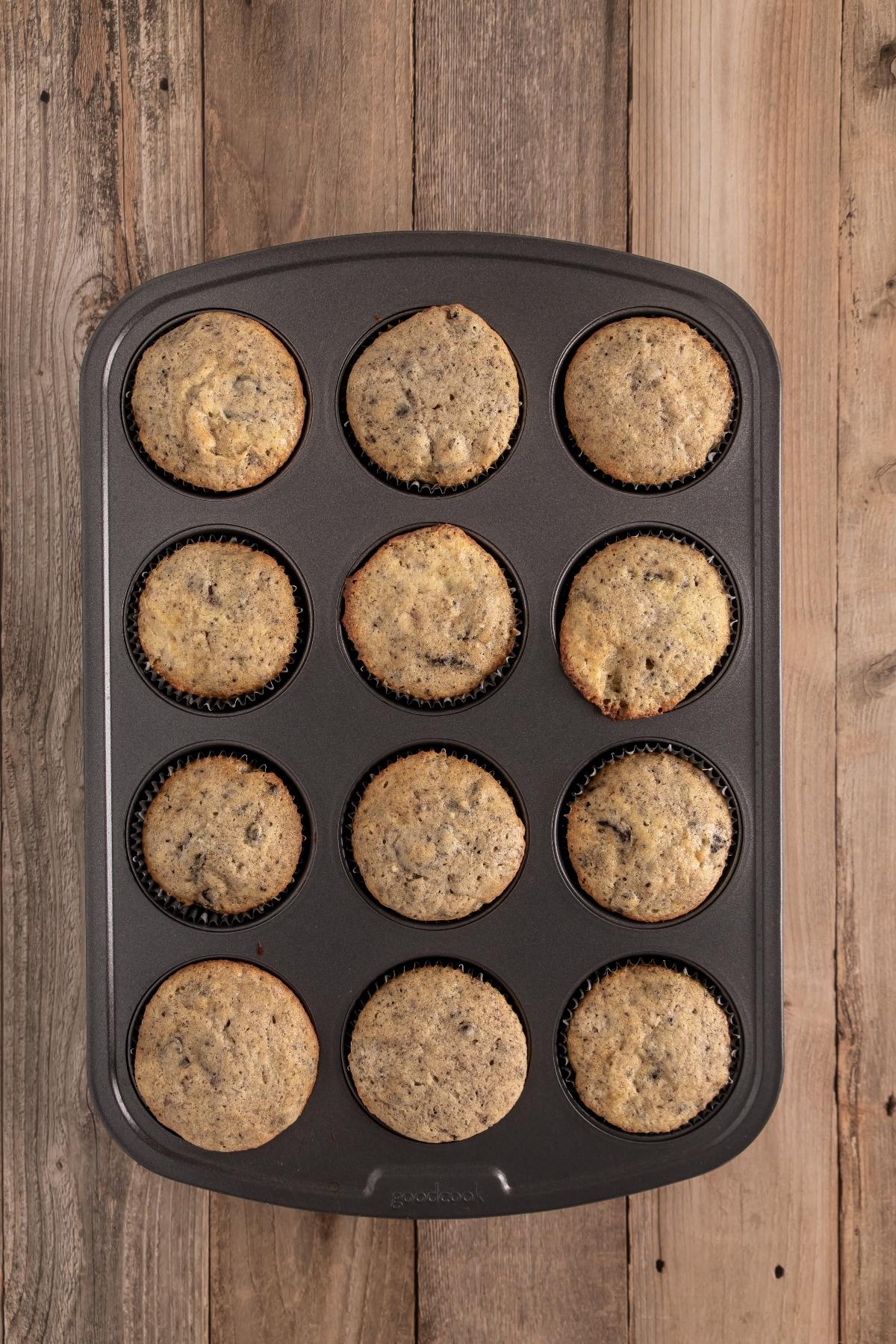A muffin tray with twelve baked muffins sits on a wooden surface.