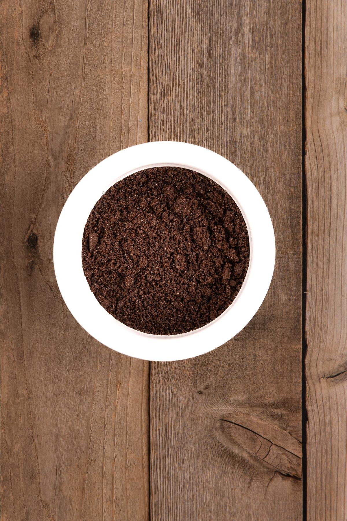 A white bowl filled with ground coffee on a wooden surface, viewed from above.