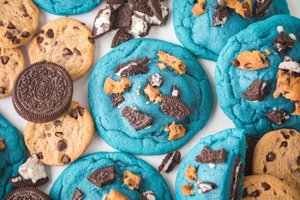 Oreo Stuffed Cookie Monster Cookies: Blue cookies topped with Oreo and chocolate chip pieces, surrounded by whole cookies and crumbs.