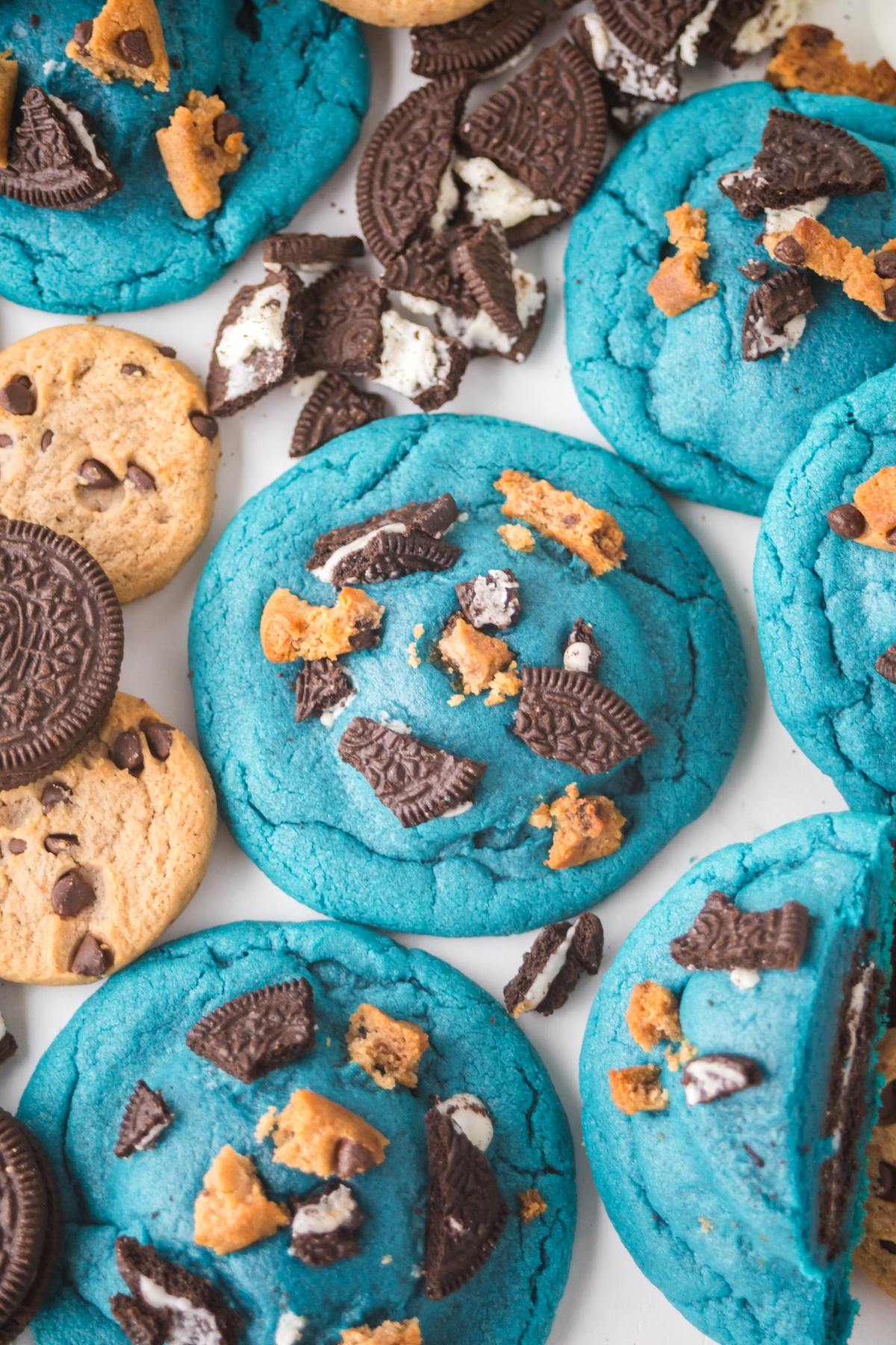Bright blue cookies topped with crumbled chocolate sandwich cookies and chocolate chip cookies, seen close up.
