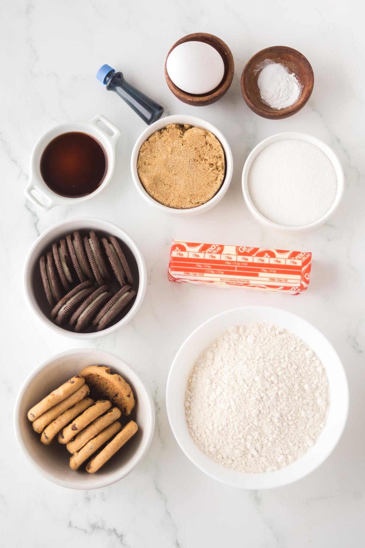 Various baking ingredients in bowls, including cookies, flour, sugar, butter, eggs, and vanilla extract.
