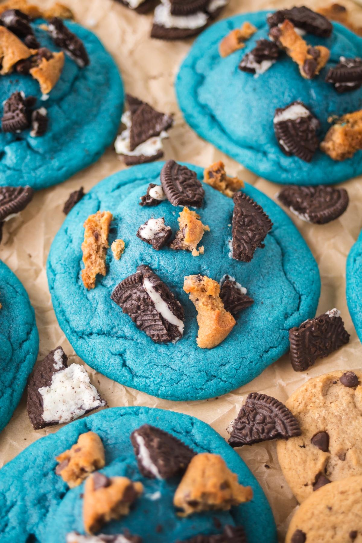 Bright blue cookies topped with cookie crumbles and chocolate sandwich cookie pieces on parchment paper.