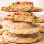 A stack of colorful Oreo Stuffed Funfetti Cookies, some whole and some broken in half, with rainbow sprinkles.