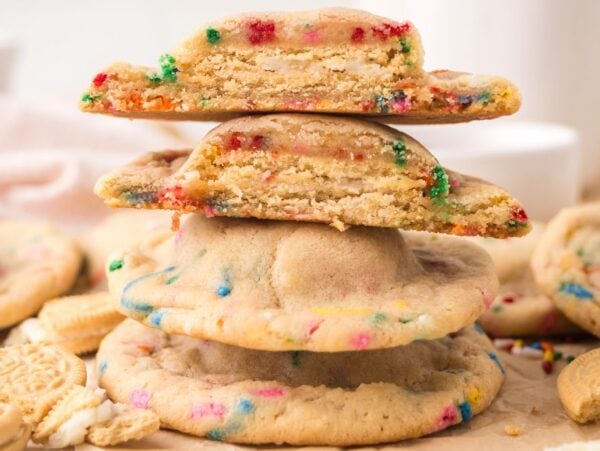 A stack of colorful Oreo Stuffed Funfetti Cookies, some whole and some broken in half, with rainbow sprinkles.