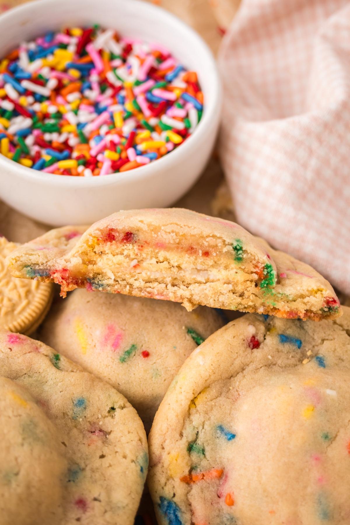 A close-up of funfetti cookies with colorful sprinkles and a bowl of assorted sprinkles in the background.