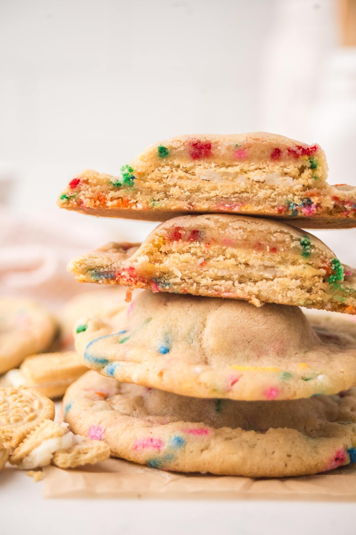 A stack of colorful confetti cookies, with one cookie broken in half on top, showing its soft inside.