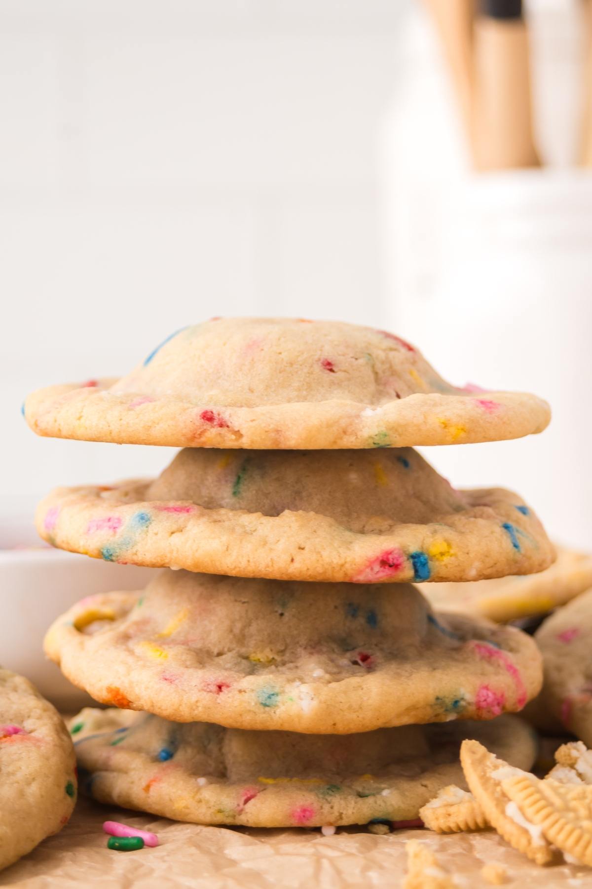 Three thick, round cookies with colorful sprinkles are stacked on parchment paper.