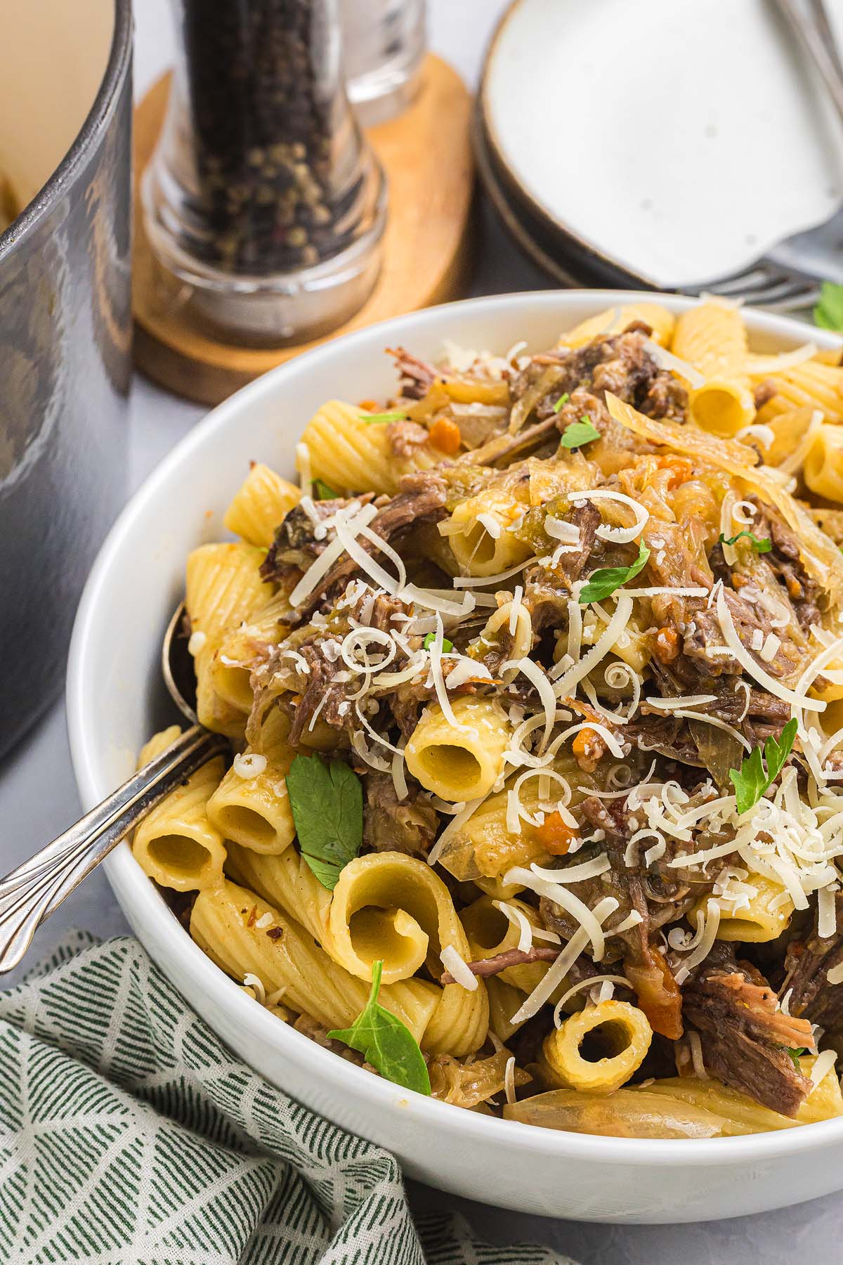 A bowl of pasta alla Genovese featuring rigatoni with shredded beef, grated cheese, and fresh basil leaves.